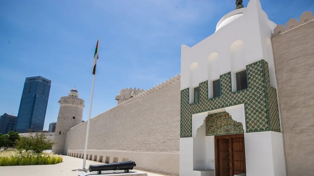 Qasr Al Hosn fort entrance with UAE flag and modern skyscraper in Abu Dhabi.