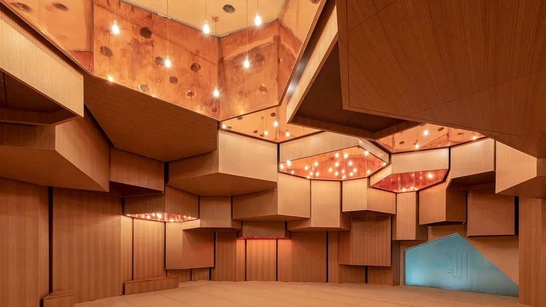 Interior of Qasr Al Hosn auditorium with geometric wooden panels and warm lighting.