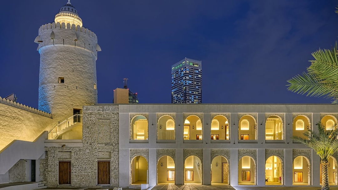 Qasr Al Hosn illuminated at night, Abu Dhabi, with modern skyscrapers in the background.
