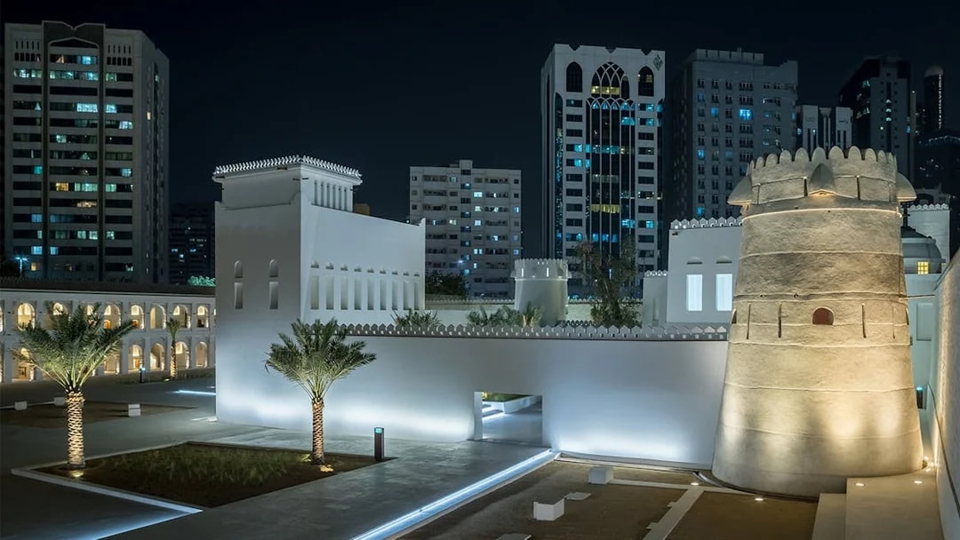 Qasr Al Hosn fortress illuminated at night in Abu Dhabi, with modern buildings in the background.