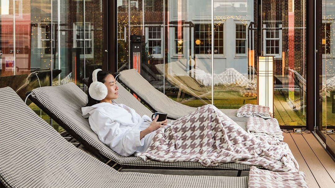 Person relaxing on a lounge chair with a blanket at QC New York spa.