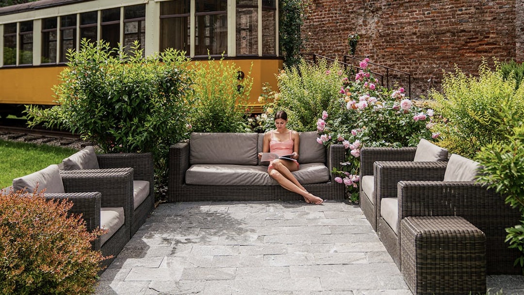 Outdoor seating area at QC Terme Milano with a woman reading, surrounded by greenery and flowers.