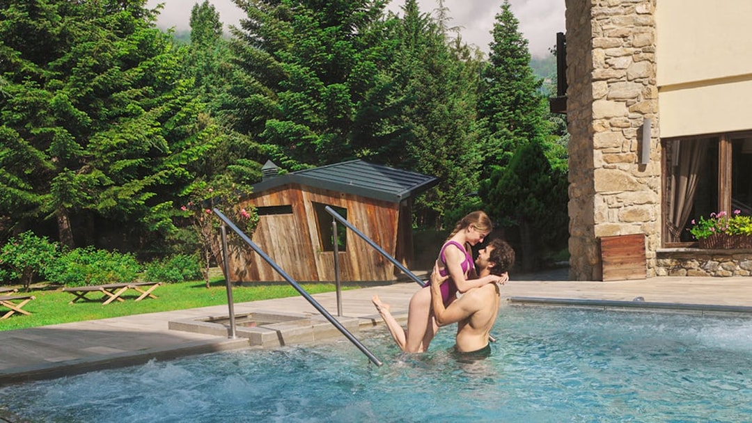 Couple enjoying outdoor pool at QC Terme Pré Saint Didier with lush greenery.