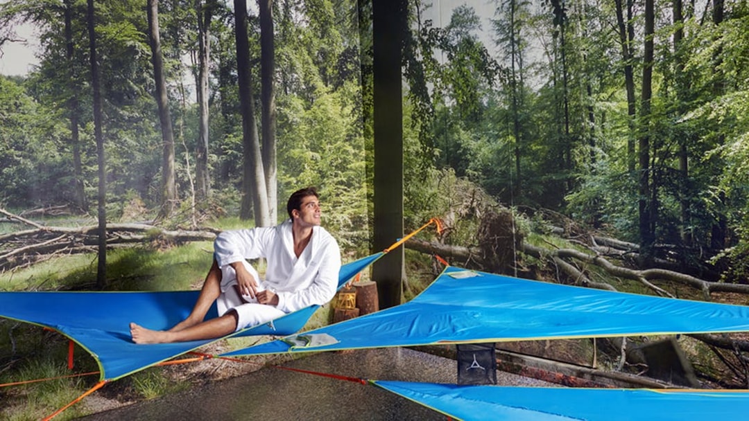 Man relaxing on a blue hammock at QC Terme Pré Saint Didier spa with forest backdrop.