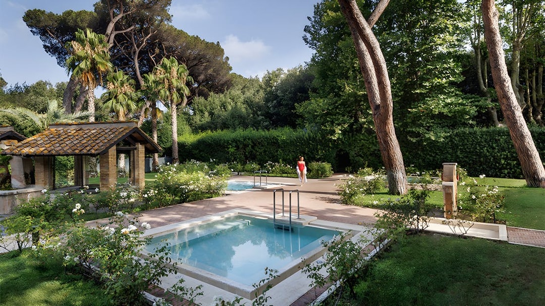Pool and gardens at QC Terme Roma Resort & Spa, Italy, surrounded by lush greenery.