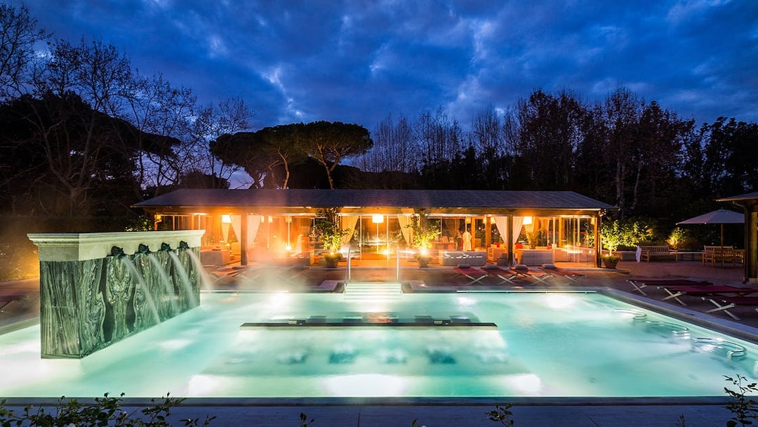 Outdoor thermal pool at QC Terme Roma with illuminated spa area at dusk.