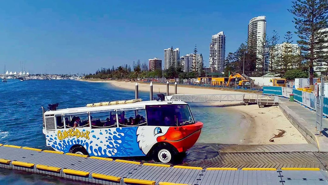 Quack'R Duck amphibious vehicle entering water at Gold Coast with city skyline in background.