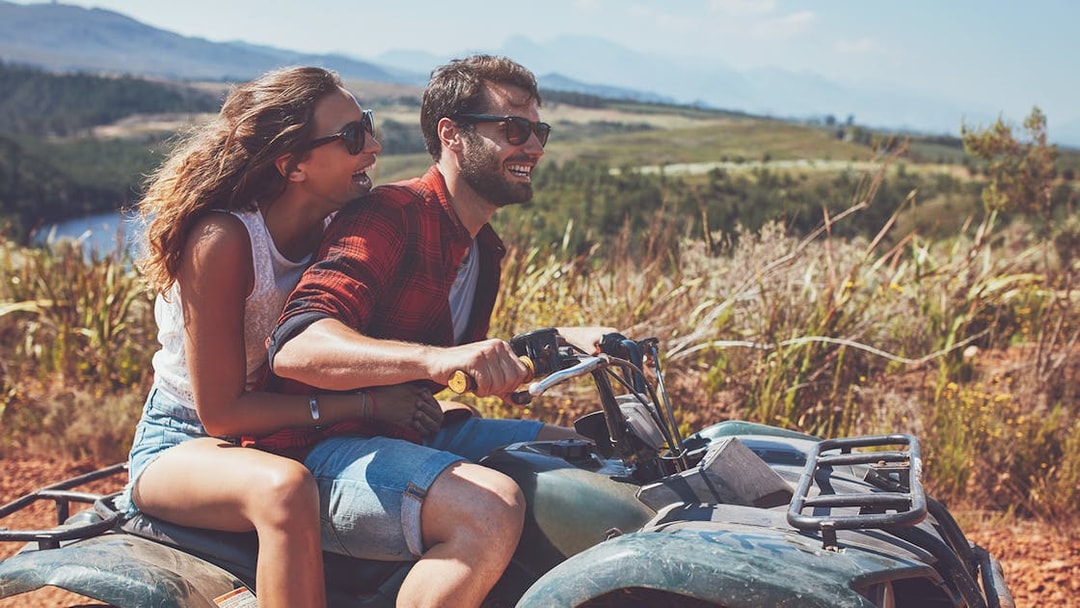Couple riding an ATV during a quad safari in Antalya, with scenic landscape in the background.