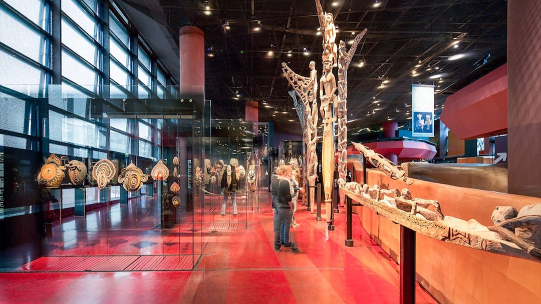 Musee du Quai Branly interior with tribal art displays and visitors exploring exhibits.