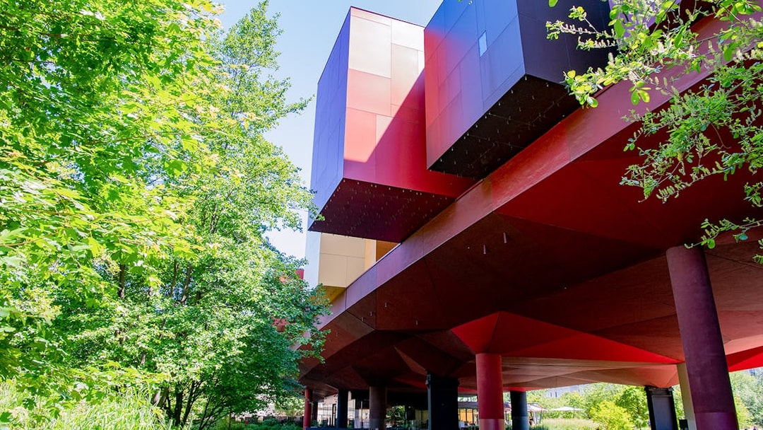 Musee du Quai Branly building with vibrant red and orange facade surrounded by greenery in Paris.