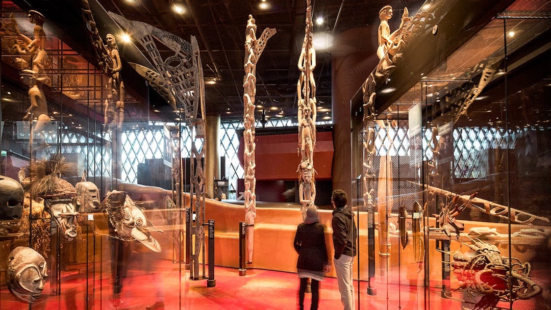 Musee du Quai Branly interior with visitors viewing tribal masks and sculptures.