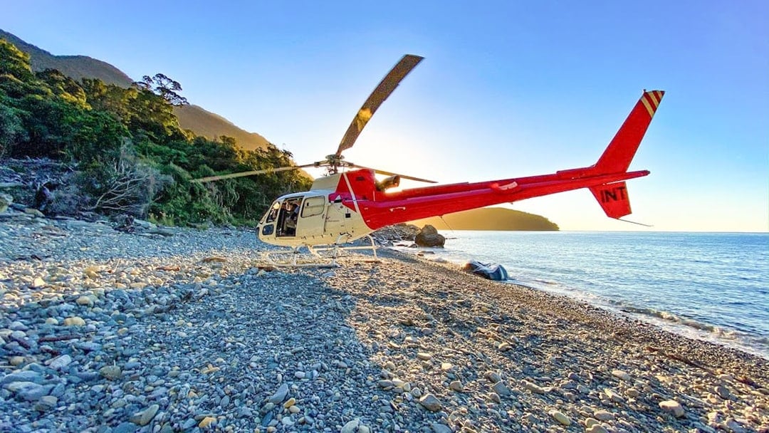 Red and white helicopter on a remote beach near Milford Sound, New Zealand, during a Queenstown tour.
