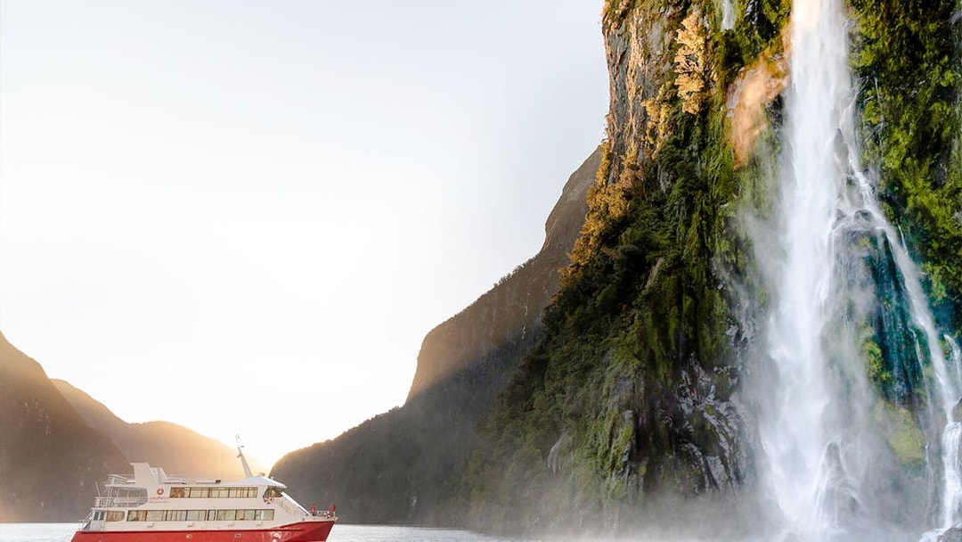 Cruise boat near waterfall in Milford Sound, New Zealand.