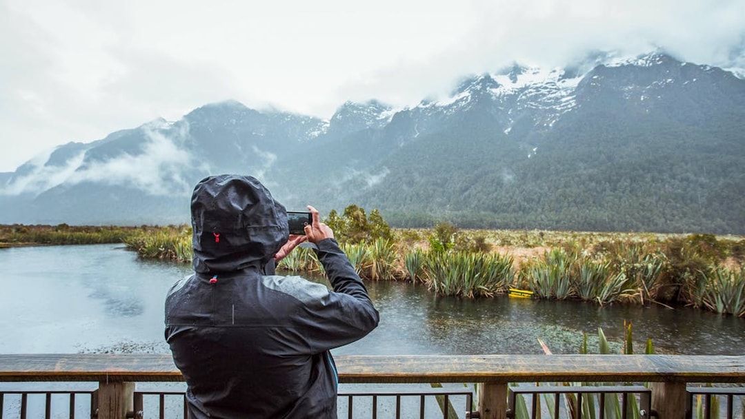 Person photographing misty mountains and lake in Milford Sound, New Zealand.