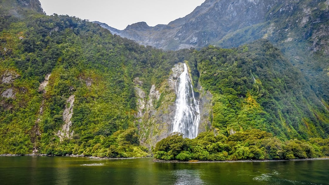 Waterfall cascading down lush green mountains in Milford Sound, Queenstown day trip.