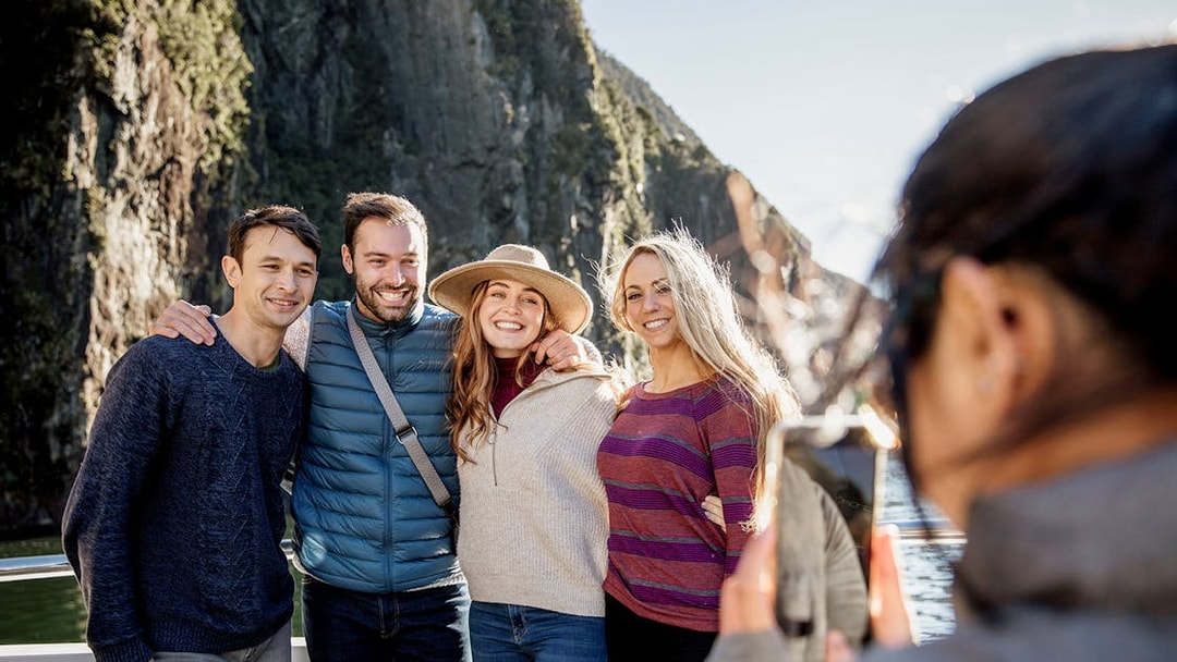 Group posing on Milford Sound cruise with cliffs in background, Queenstown day trip.