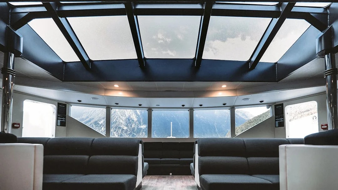 Interior of a cruise ship with panoramic windows showcasing Milford Sound mountains.