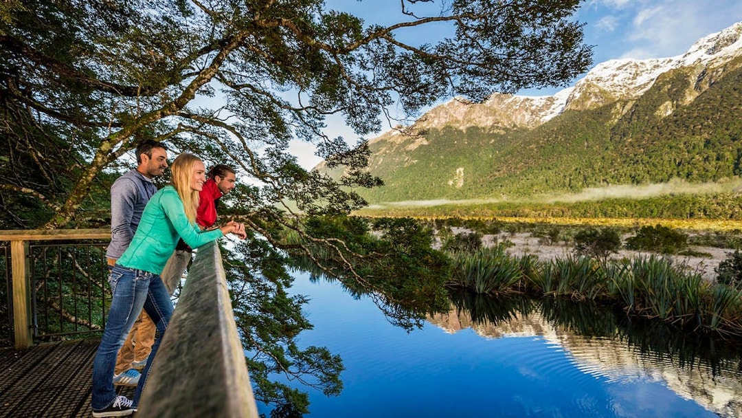 Visitors enjoying the view at Mirror Lakes, New Zealand, with mountains reflected in the water.