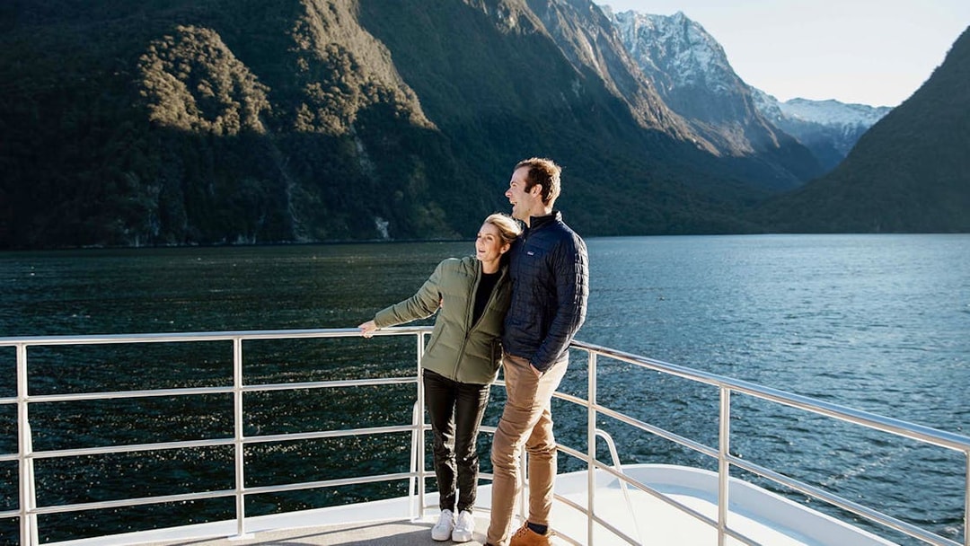 Couple enjoying Milford Sound views from a cruise deck, surrounded by mountains and water.