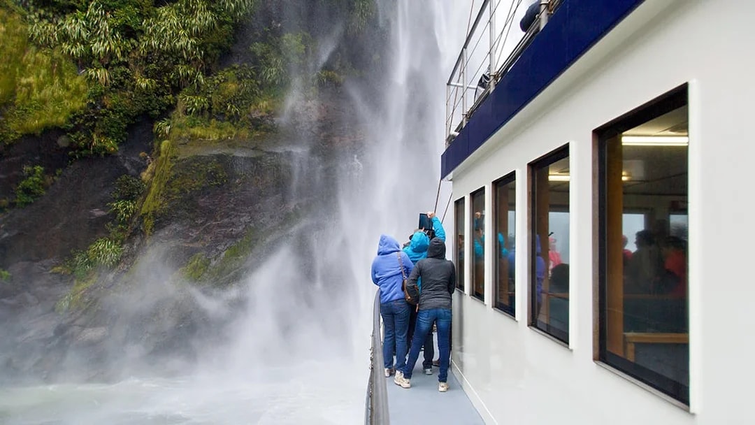 Tourists on a boat viewing a waterfall at Milford Sound, New Zealand.