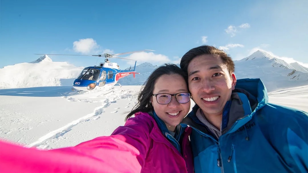 Couple on snow-covered mountain with helicopter during Queenstown Panorama Helicopter Tour.