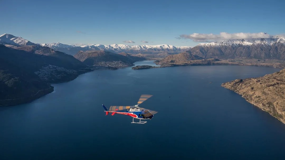 Helicopter flying over Lake Wakatipu with snow-capped mountains in Queenstown, New Zealand.