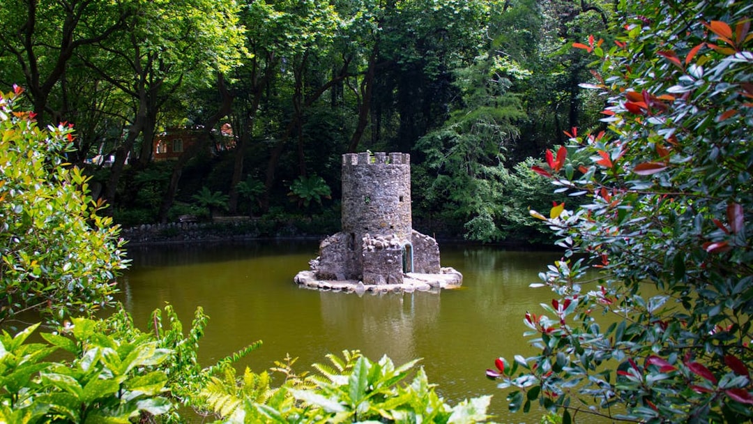 Stone tower surrounded by lush greenery in the gardens of Quinta da Regaleira, Sintra, Portugal.