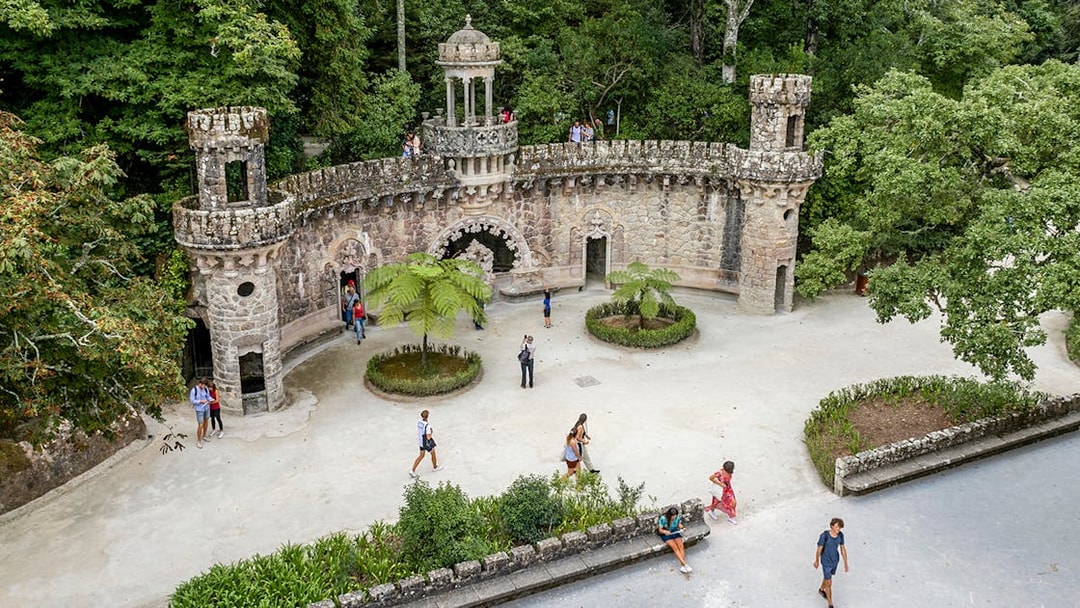Guided tour group exploring gardens at Quinta da Regaleira, Sintra, near stone structure.