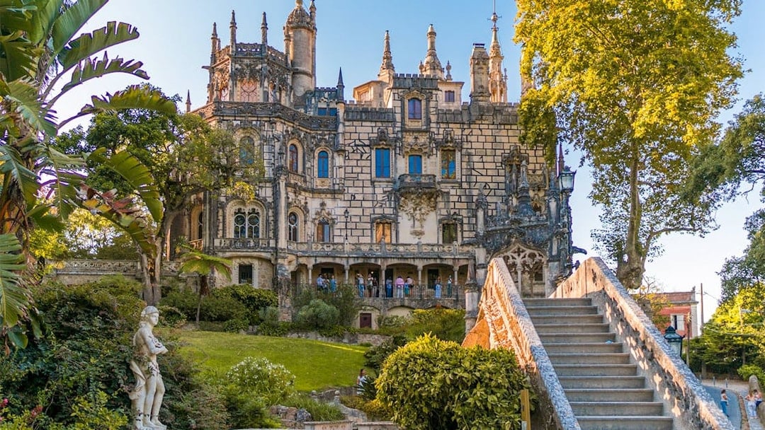 Quinta da Regaleira exterior with ornate architecture, garden, and stone staircase in Sintra, Portugal.