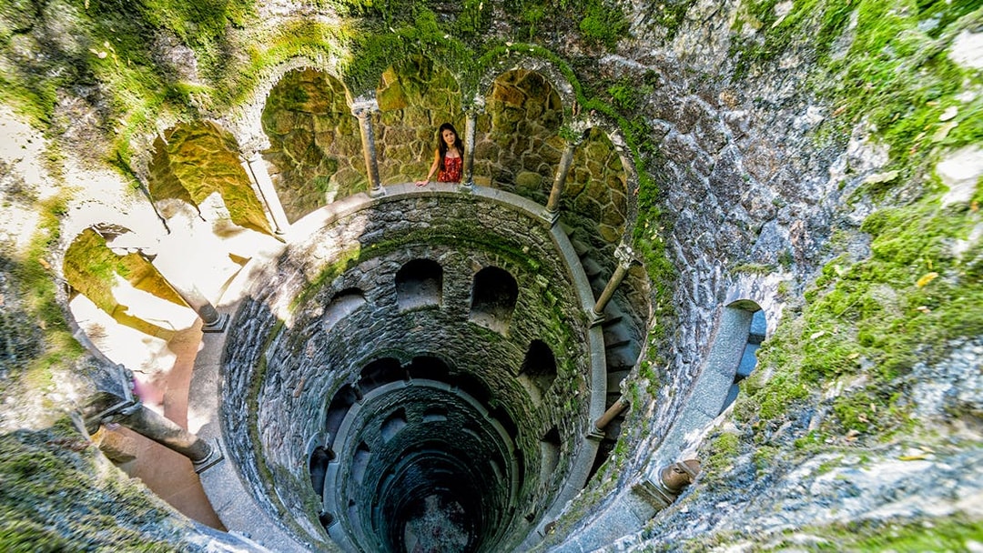 Initiation Well at Quinta da Regaleira, Sintra, Portugal with spiral staircase and moss-covered walls.