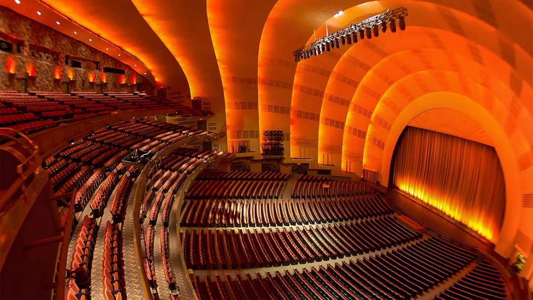 Interior of Radio City Music Hall with empty seats and illuminated stage.