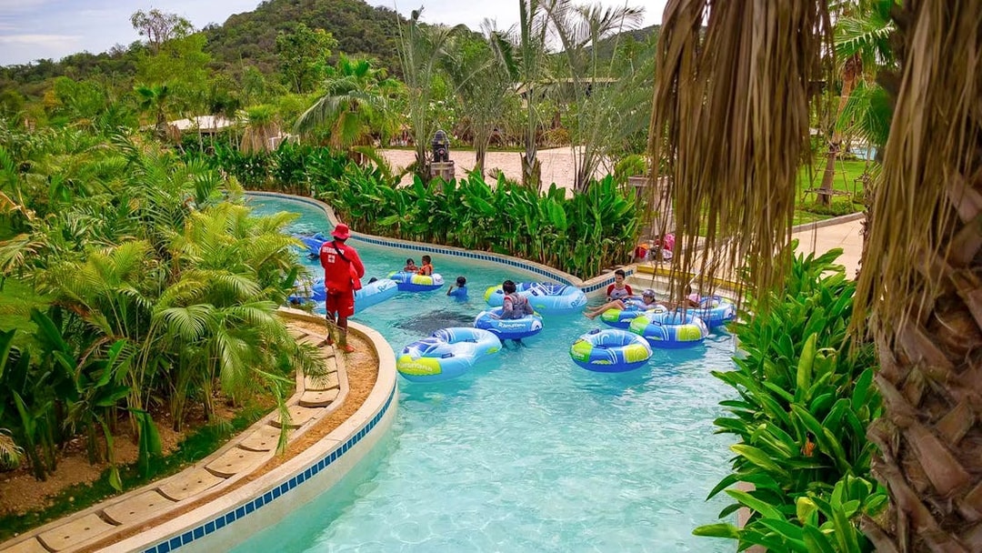Visitors floating on inflatable tubes in a lazy river at Ramayana Water Park, surrounded by lush greenery.