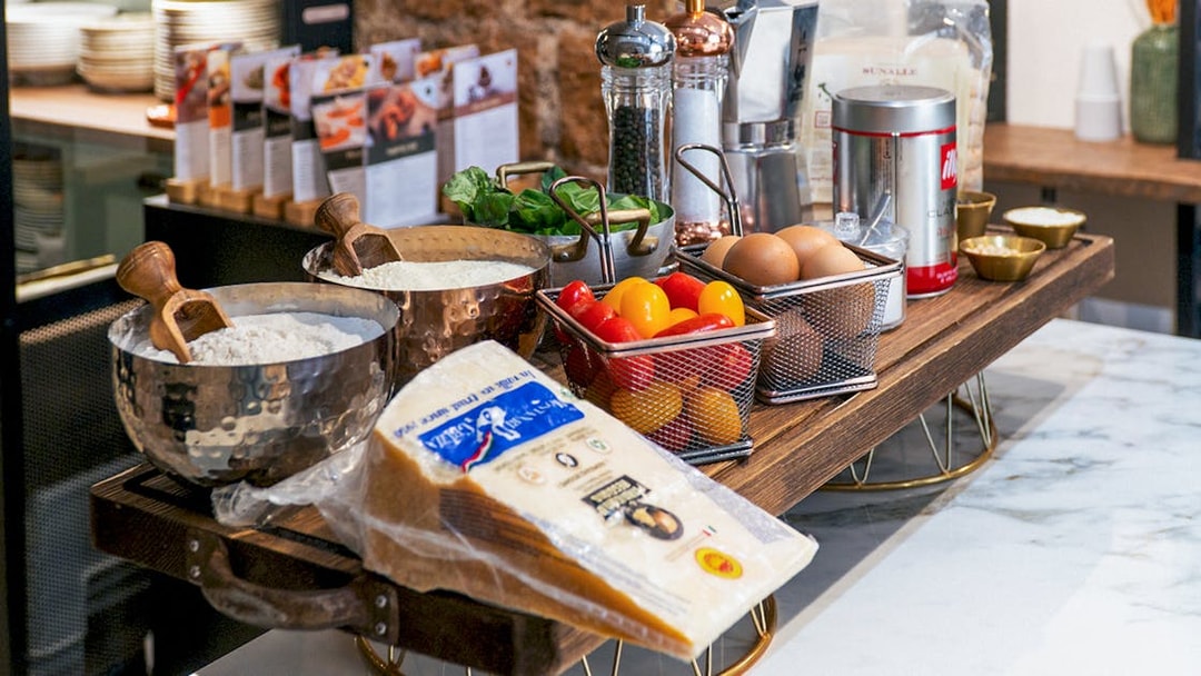 Ingredients for pasta making class including flour, eggs, cheese, and tomatoes on a kitchen counter.