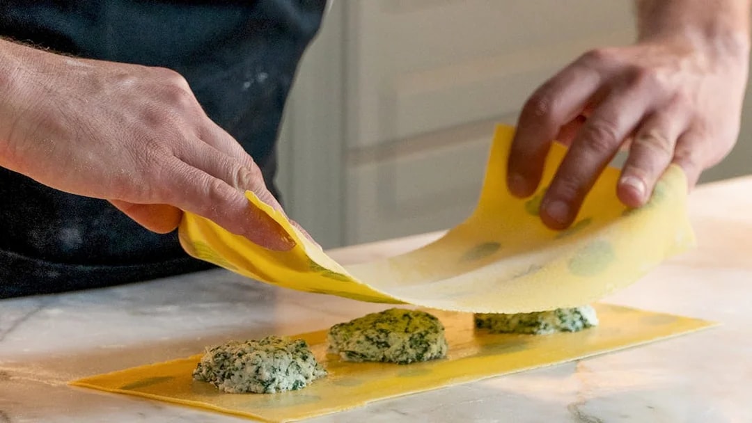 Hands preparing ravioli with spinach filling during a pasta making class.