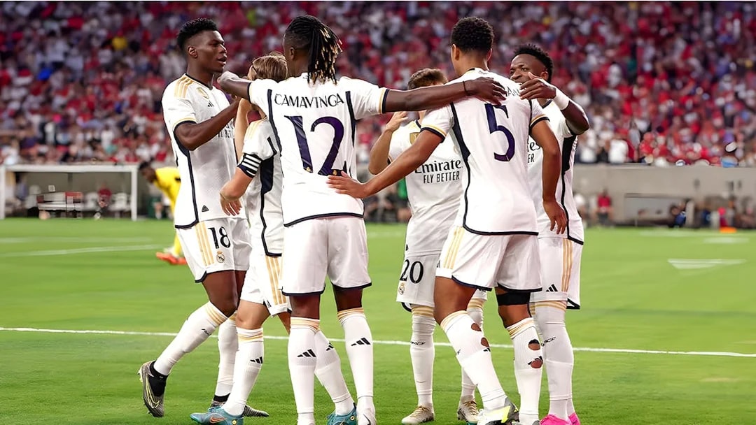 Soccer players in white jerseys huddling on a field during a match.