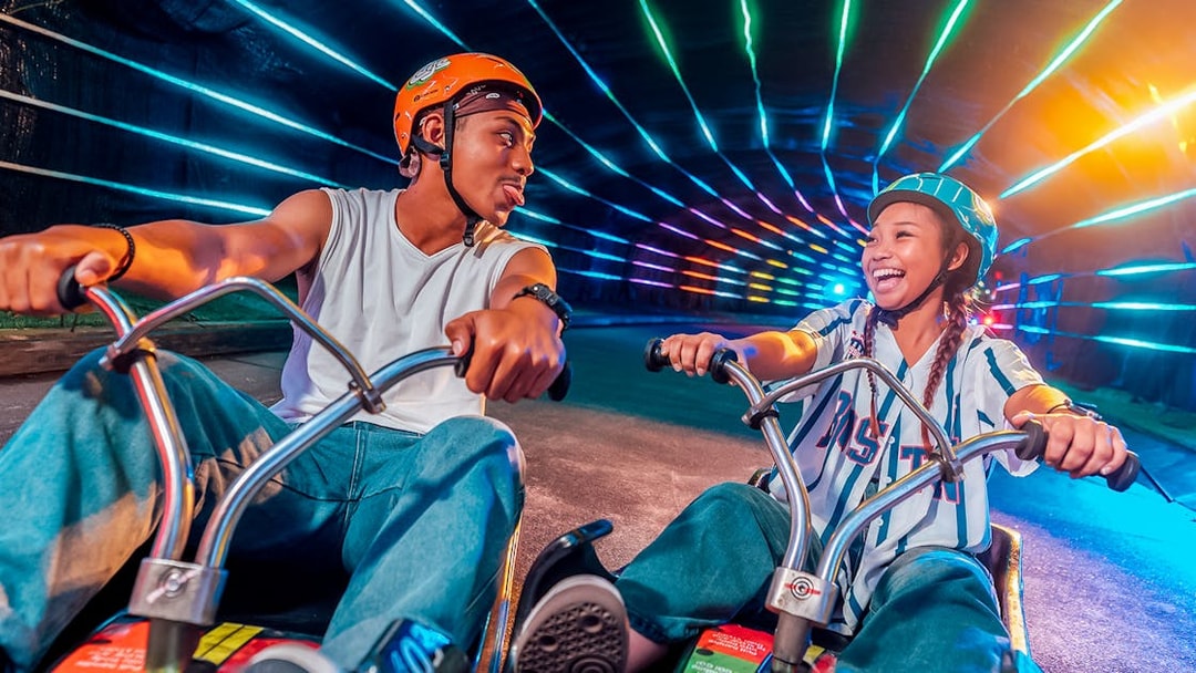 Friends enjoying night luge ride with colorful lights in Singapore.