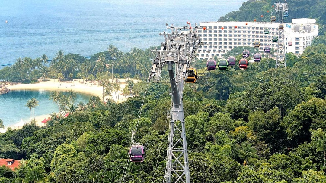 Cable cars over lush greenery and beach in Sentosa, Singapore.