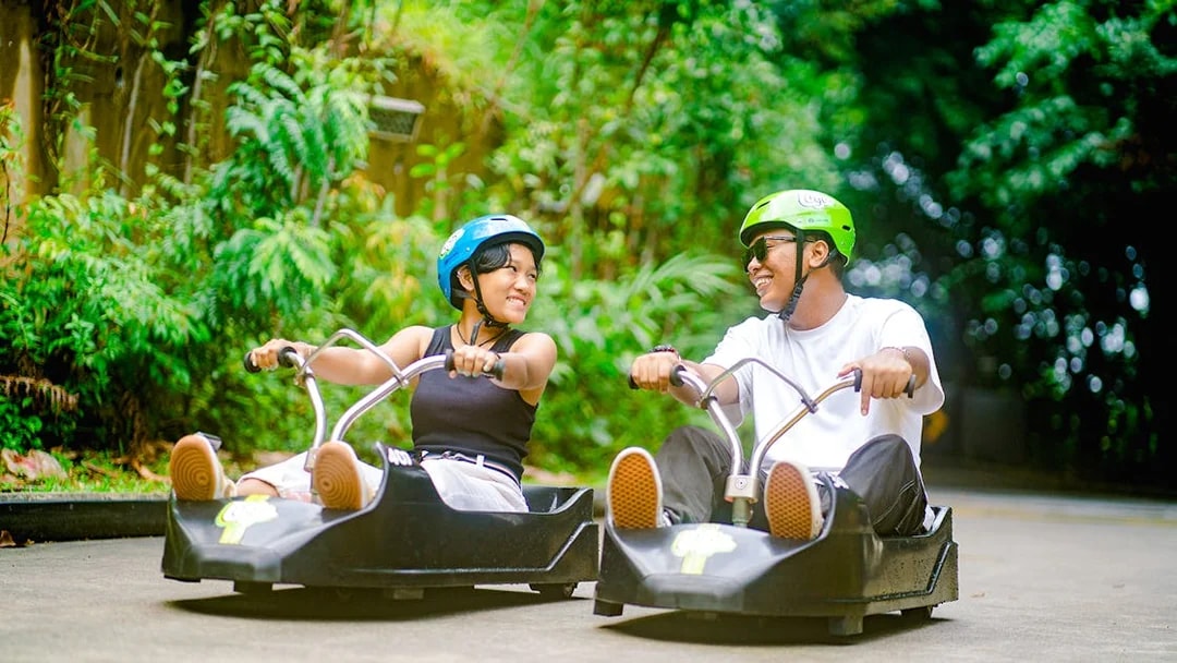 Couple enjoying Skyline Luge ride in Singapore amidst lush greenery.