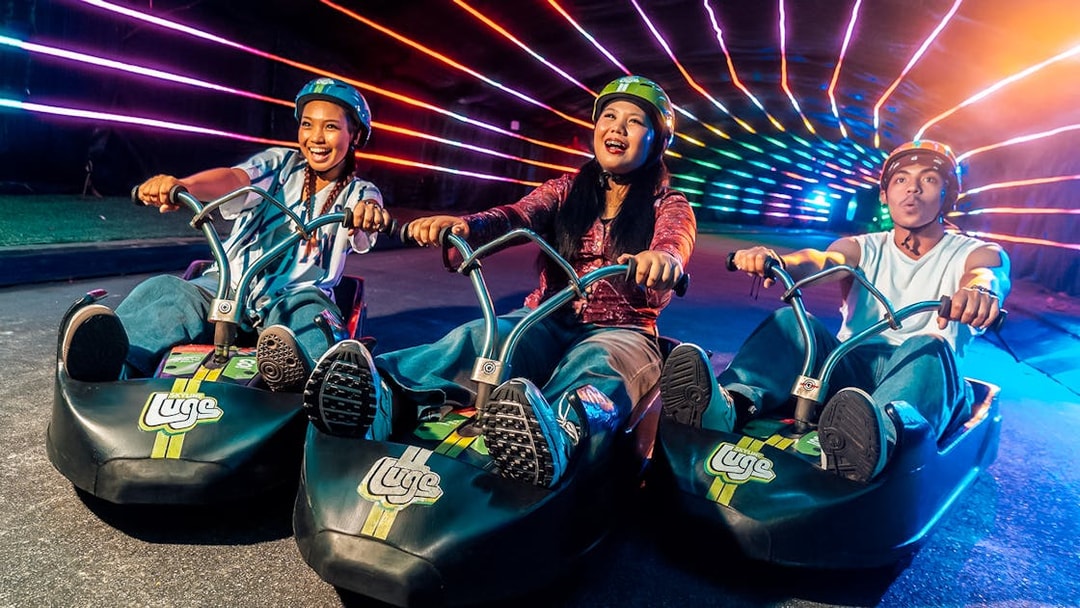 Friends enjoying night luge ride under colorful lights in Singapore.