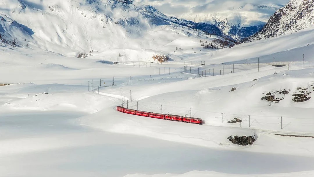 Bernina train traveling through snowy Swiss Alps landscape.