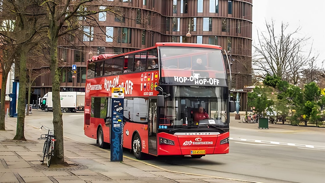 Copenhagen hop-on hop-off tour bus on city street near modern building.