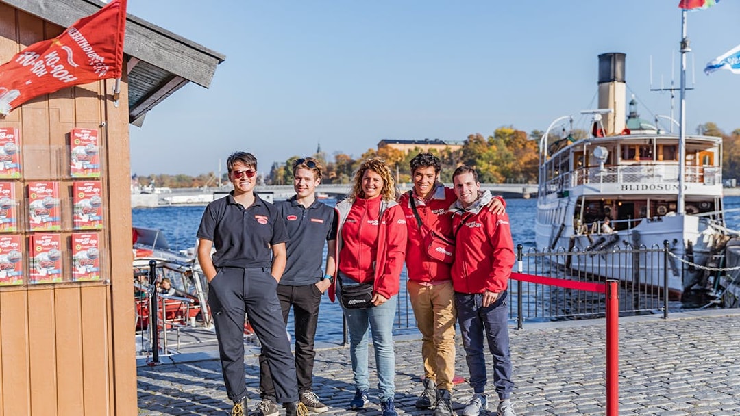 Stockholm boat tour crew standing by the waterfront with a historic ship in the background.