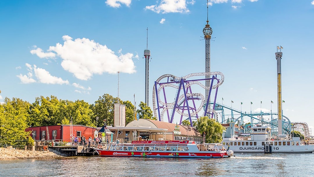 Stockholm sightseeing boat near amusement park rollercoaster on a sunny day.