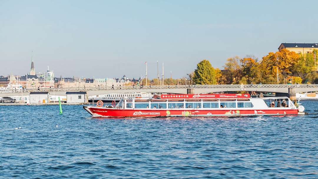 Stockholm sightseeing boat on water near cityscape and bridge.