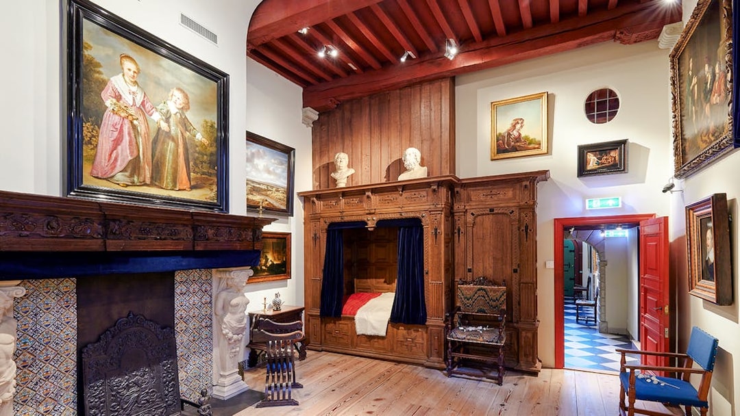 Interiors of the Rembrandt House Museum featuring a wooden bed, fireplace, and paintings.