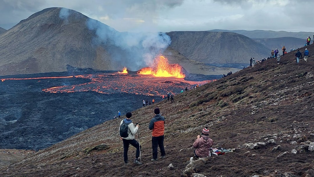 Hikers observing volcanic eruption and lava flow in Reykjanes, Iceland.