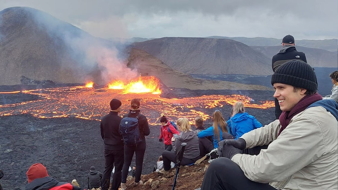 Tourists observing volcanic eruption at Reykjanes, Iceland, with visible lava flow.