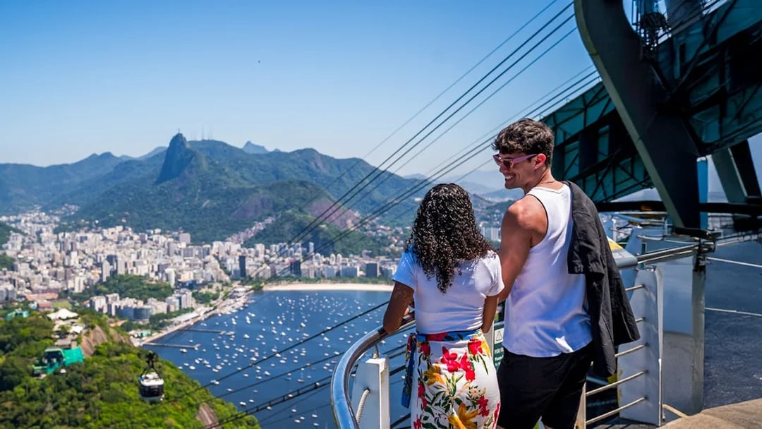 Cable cars descending from Sugarloaf Mountain with a view of Rio de Janeiro and Guanabara Bay.