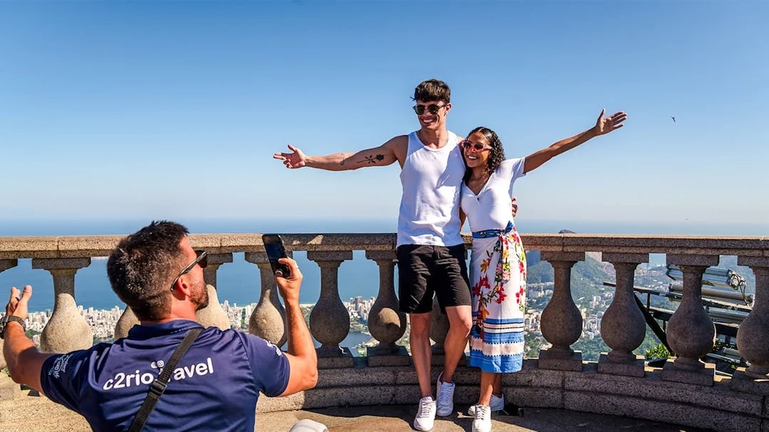 Couple posing at Christ the Redeemer viewpoint, Rio de Janeiro, with cityscape in background.