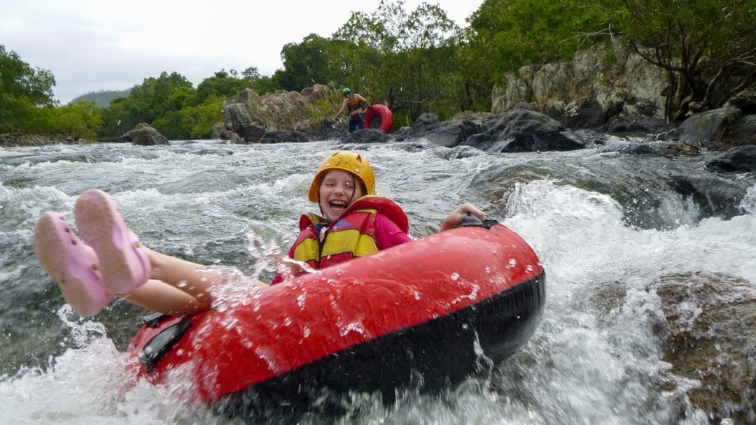 Child enjoying river tubing adventure through rapids, wearing safety gear.
